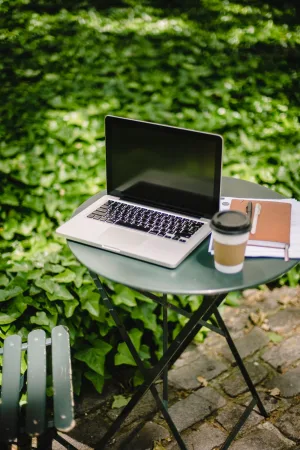 Laptop, notebook and takeaway coffee on a table outside.