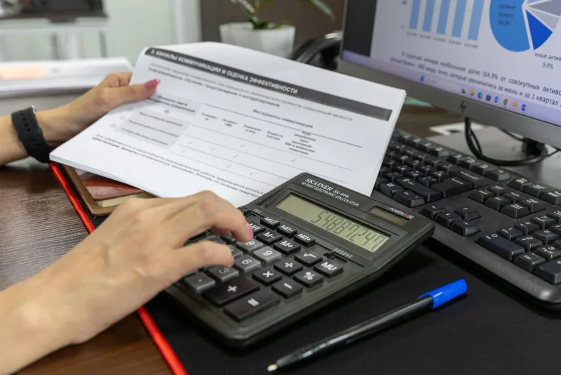 Hands using a calculator while reviewing a financial document at a desk.
